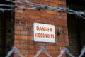 Danger 11,000 volts sign on brick wall surrounded by barbedwire. High voltage Royalty Free Stock Photo