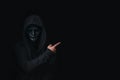 Dangerous anonymous hacker man in hooded and mask break security data and hack password with Bank account. He pointing away on bla