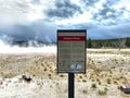 Dangerous Ground Sign in Front of an Active Geyser with Rising Steam in Yellowstone Royalty Free Stock Photo