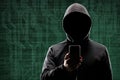 Dangerous hacker with a smartphone gadget over digital background with binary code. Obscured dark face in mask and hood Royalty Free Stock Photo