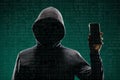 Dangerous hacker with a smartphone gadget over digital background with binary code. Obscured dark face in mask and hood Royalty Free Stock Photo