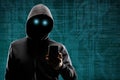 Dangerous hacker with a smartphone gadget over digital background with binary code. Obscured dark face in mask and hood Royalty Free Stock Photo