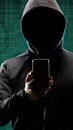 Dangerous hacker with a smartphone gadget over digital background with binary code. Obscured dark face in mask and hood. Data Royalty Free Stock Photo