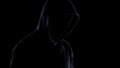 Dangerous maniac in mask and hoodie standing against black background, crime