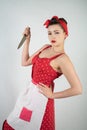 Dangerous pin up girl housewife in red vintage polka dot dress stands with a huge kitchen knife in her hands and angrily rejoices