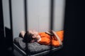 A dangerous prisoner in a cell rests and sleeps in a solitary cell on a bunk in an orange robe.