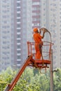 Dangerous work concept. Vertical photo employee workman in orange formal wear uniform stand in lift bucket changing light bulb or