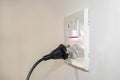 The dangers of using electricity in the home include a black plug that is not completely plugged into the white wall.