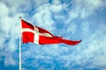 Danish Flag, the Dannebrog, in front of a blue and cloudy sky. Royalty Free Stock Photo