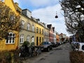 Danish street with colorful townhouses, old trees, parked cars and bicycles