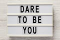 `Dare to be you` on a lightbox on a white wooden background, top view. Flat lay, overhead, from above. Close-up