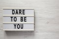 `Dare to be you` on a lightbox on a white wooden background, top view. Flat lay, overhead, from above. Copy space