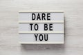 `Dare to be you` on a lightbox on a white wooden surface, top view. Flat lay, overhead, from above