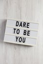 `Dare to be you` on a lightbox on a white wooden surface, top view. Flat lay, overhead, from above