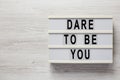 `Dare to be you` on a lightbox on a white wooden surface, top view. Flat lay, overhead, from above. Space for text