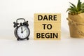 Dare to begin symbol. Wooden blocks with words `Dare to begin`. Beautiful white background, black alarm clock, house plant.