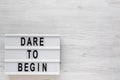 `Dare to begin` words on a lightbox on a white wooden surface, top view. Overhead, from above, flat lay. Copy space