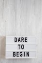 `Dare to begin` words on a lightbox on a white wooden surface, top view. Overhead, from above, flat lay. Copy space