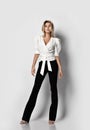 Daring tall blonde slim woman model in office pantsuit shirt with deep neckline and pants stands with legs spread wide Royalty Free Stock Photo