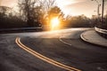 Dark asphalt road with bright yellow lines curves under sunset