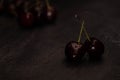 Dark atmospheric image of two ripe red cherries with crossed stems and a pile of cherries in the background on a dark metalic