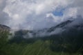 Dark atmospheric surreal landscape with a dark rocky mountain peak in low clouds in a gray cloudy sky Royalty Free Stock Photo