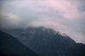 Dark atmospheric surreal landscape with a dark rocky mountain peak in low clouds in a gray cloudy sky Royalty Free Stock Photo