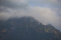 Dark atmospheric surreal landscape with a dark rocky mountain peak in low clouds in a gray cloudy sky Royalty Free Stock Photo