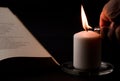 candles with flame, man\'s hand with lighter, and reading book on desk, black background. (focus on candle).
