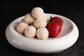 On a dark background, coconut sweets and strawberries in a light plate