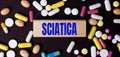 On a dark background, multi-colored pills and the word SCIATICA on a wooden block. Medical concept