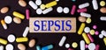 On a dark background, multi-colored pills and the word SEPSIS on a wooden block. Medical concept