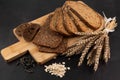 On a dark background on a wooden board are different types of bread, ears of wheat Royalty Free Stock Photo