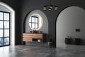 Dark bathroom interior with concrete floor, arches, black toilet and oval mirror