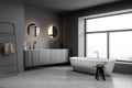 Dark bathroom interior with white bathtub and large window