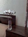 on the dark bedside table there is a glass vase with a bouquet of cotton flowers