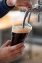 Dark beer in plastic cup flowing from beer tap with nice foam close-up in female bartender hands