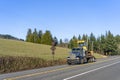 Dark big rig semi truck transporting tractor on flat bed semi trailer running on the road with field on the hill Royalty Free Stock Photo