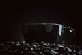 A dark black coffee cup is placed over a pile of roasted coffee beans with a black background Royalty Free Stock Photo