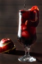 A dark blood cocktail with ice and a red apple, in a tall glass, on a dark background, a symbol of bloodshed in the war, death