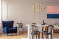 Dark blue armchair in a dining room interior with a table, chairs and golden lamp