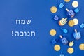 Dark blue background with multicolor dreidels and chocolate coins and Happy Hanukkah wording in Hebrew Royalty Free Stock Photo