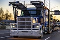 Dark blue classic big rig car hauler semi truck transporting cars on modular semi trailer running on the highway road at twilight Royalty Free Stock Photo