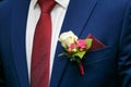 Dark blue groom`s suit and boutonniere of white and red roses