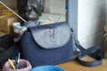 A dark blue knitted bag with a leather insert and an elephant print on a light wooden surface. Workplace in the process of Royalty Free Stock Photo