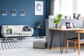 Dark blue living room interior with three clocks, simple poster, bright sofa and home office corner with laptop on hairpin desk Royalty Free Stock Photo