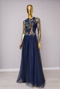 Long, blue designer, evening, women`s dress handmade on gold, glossy mannequin. With white and gold ornament in