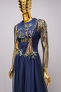 Long, blue designer, evening, women`s dress handmade on gold, glossy mannequin. With white and gold ornament in