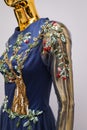 Long, blue designer, evening, women`s dress handmade on gold, glossy mannequin. With white and gold ornament in