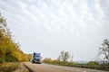 Dark blue long haul big rig semi truck with semi trailer running on winding autumn road Royalty Free Stock Photo